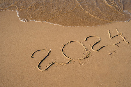 New Year concept. Text 2024 handwritten in sand surface. Blue ocean wave washing away numbers at the beach. Welcoming year 2024 Happy New Year coming new resolutionsの写真素材