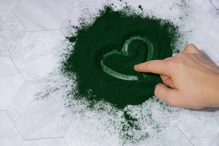 Female hand draw heart on Blue-green algae Chlorella and spirulina powder. Super powder. Natural...
