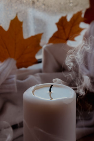 Thanksgiving and Hello Fall Halloween concept Celebrating autumn holidays at cozy home on the windowsill Hygge aesthetic atmosphere Autumn leaves spices and candle on knitted white sweater in warm yellow lightsの写真素材