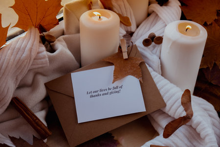 LET OUR LIVES BE FULL OF THANKS AND GIVING text greeting card concept Celebrating autumn holidays at cozy home on the windowsill Hygge aesthetic atmosphere Autumn leaves spices and candle on knitted white sweater in warm yellow lights. Still life.の写真素材