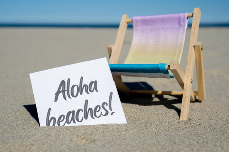 ALOHA BEACHES text on paper greeting card on background of beach chair lounge summer vacation decor. Sandy beach sun. Holiday concept postcard. Travel