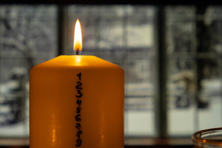 Candle with advent calendar on windowsill window with snowy weather outdoor. Traditional Burning...