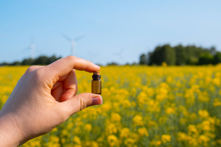 Hand holding test tube with liquid on background of canola flowers field blooming farm. Rapeseed oil...