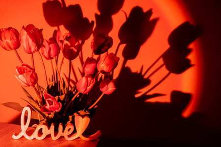 Wooden word LOVE on background of Pink colored tulip flower in neon light on red gradient background in the night light. Valentines Anniversary Holiday. Creative dark holiday concept. Copy space greeting card. Aesthetic sunset lampの写真素材