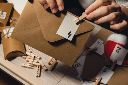 Unrecognizable young woman sticks number on craft bag, fastens with clothespin. Female making kraft paper for homemade advent calendar Made with your own hands step by step DIY crafts do it yourself. Preparation to christmas concept. Seasonal activities for children family winter holidays. Eco friendly presents giftsの写真素材
