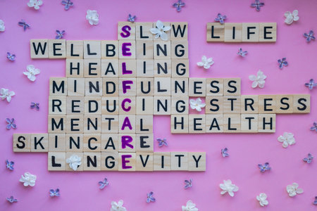 Top view of SELFCARE word on pink background with flowers. Minimalism creative crossword puzzle concept. Message of text Slow life wellbeing healing mindfulness reducing stress mental health skincare longevityの写真素材