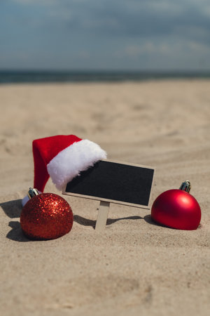 Empty blackboard frame board with copy space for your text or design displays on sandy beach. Christmas balls Santa hat New Year decoration. Summer vacation and holiday business travel concept. Template Mock up for sale promotion advertisementの写真素材