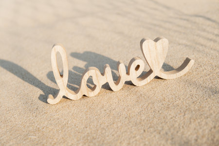Wooden word love on sandy beach background. Concept of romantic holiday anniversary, proposal, valentines day greeting card, postcard. Letter text in tropical vacation Sand surfaceの写真素材