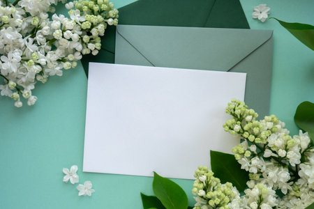 Composition with empty green envelope and beautiful spring lilac flowers on mint background. Mockup card invitation greeting card postcard copy space template. Branches of lilac blooming bouquet.の写真素材