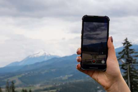Mobile phone shooting video for social media. Tourist blogger travel hand making memories Snowy mountains, green forests In National park. Mountain nature landscape. Travel outdoors green tourism concept Naturecoreの写真素材