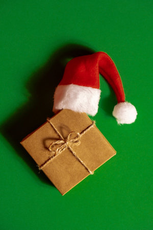 Santa hat on paper gift box present on green background. Copy space for your text. Mock up for advertisement. Holiday Christmas compositionの写真素材