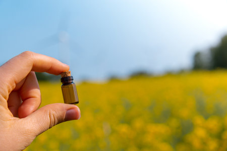 Hand holding test tube with liquid on background of canola flowers field blooming farm. Rapeseed oil over natural background. Farmer soil sample in tube chemical analysis ph test. Agrochemical analysis soil quality monitoring conceptの写真素材