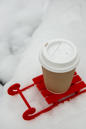 Small Red sled with paper cup of coffee or hot chocolate on snow background in beautiful winter day. Copy space for text. Mock up for product greeting card or wallpaper. Christmasの写真素材