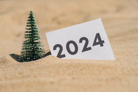 2024 text on paper greeting card on background sandy beach sun coast. Christmas tree New Year New Me decoration. Summer vacation decor. Holiday concept calendar date postcard. Getting awayの写真素材