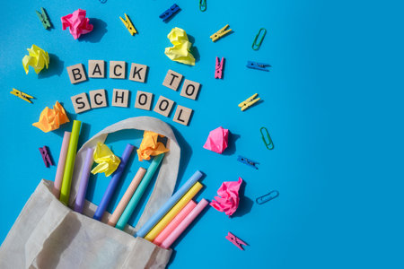 BACK TO SCHOOL message inscription text on wooden blocks on creative colorful blue background with stationery supplies around. Copy space Educational greeting announcement for students and teacher. Top view flat lay New school yearの写真素材