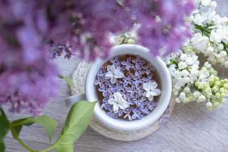 Tasty black tea in white cup on windowsill with aromatic lilac flowers. Spring composition Cup of...
