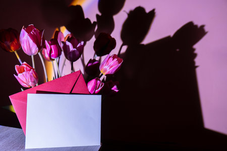 Empty envelope for your text mock up on background of Pink colored tulip flower in neon light on violet gradient background in the night light. Creative dark holiday concept. Copy space greeting card. Aesthetic sunset lampの写真素材