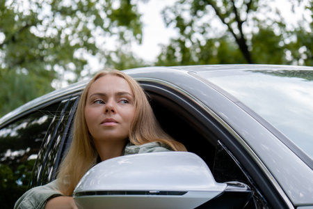 Smiling young woman looking from car window. Local solo travel concept. Exited woman explore freedom outdoors in forest. Unity with nature lifestyle, rest rechargeの写真素材