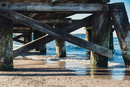 Storm sea waves under wooden pier in dramatic background wallpaper design. Seascape with running splashing sea waves. Sandy beach vacation getaway in Gdansk Polandの写真素材