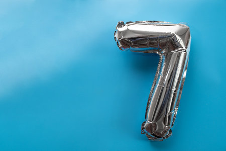 7 seven metallic balloon isolated on blue background. Greeting card silver foil balloon number Happy birthday holiday concept. Copy space for text. Celebration party congratulationの写真素材