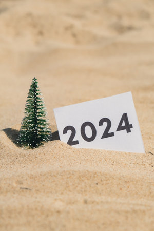 2024 text on paper greeting card on background sandy beach sun coast. Christmas tree New Year New Me decoration. Summer vacation decor. Holiday concept calendar date postcard. Getting awayの写真素材