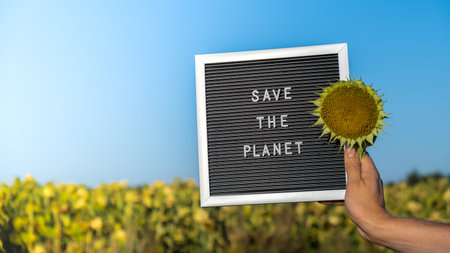 Unrecognizable person with banner message SAVE THE PLANET in sunflower field on sunny day. Sign EARTH day. Concept of ecology and eco activism environmental issues Stop global warming. Go greenの写真素材