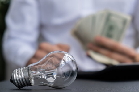 Electric light bulb. Man hands counting expenses on electricity banknotes of dollar cash accounting on calculator. Close up of hands unrecognizable Businessman. High prices for energy. Save up budget investment concept Planning budget and estimating costs billsの写真素材