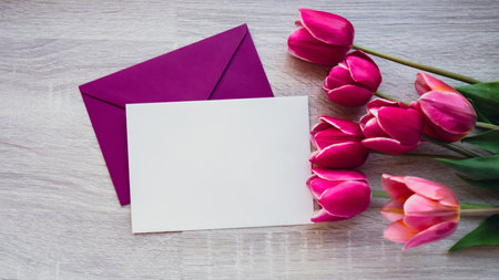 Empty white envelope copy space for your text or design with beautiful pink tulip bouquet on wooden...
