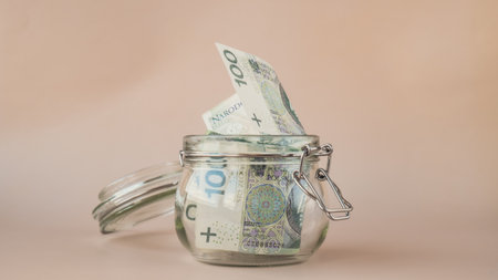 Polish zloty cash banknote in glass jar on beige background. Saving money concept crisis and...