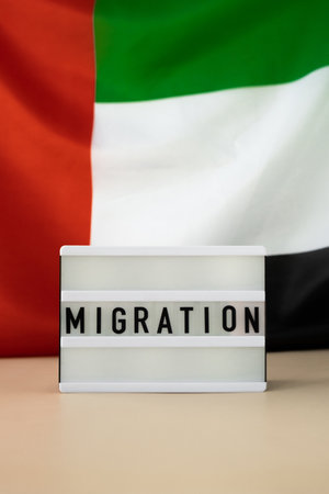 Message MIGRATION on background of UAE flag made from silk. United Arab Emirates national flag with concept of tourism and traveling. Dubai welcoming cardの写真素材