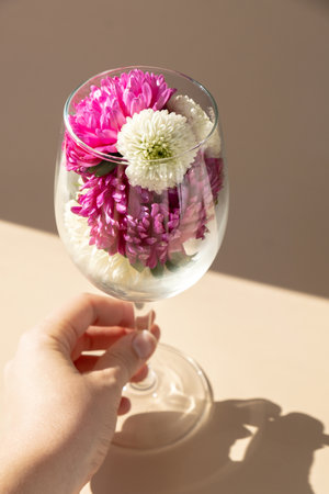 Female hand holding Wine glass full of colorful flowers. Creative concept for holidays greeting card...