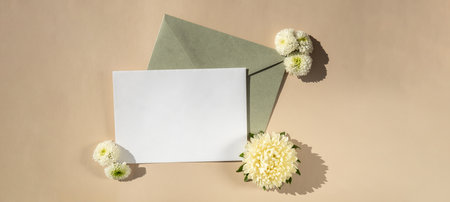 Beautiful little white flowers on postal green envelope on beige background, empty paper note copy...