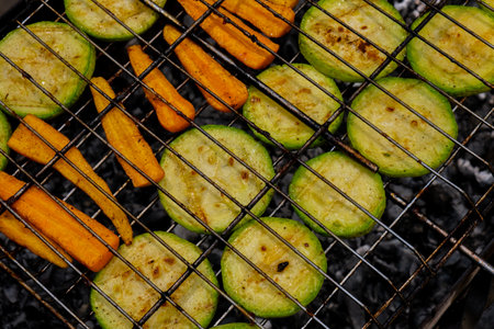 Chopped zucchini and carrots roasting on fire seasoned with aroma herbs and spices. Delicious fresh vegetables grilling on barbecue smoker grid. Diet vegan bbq. Outdoor recreationの写真素材