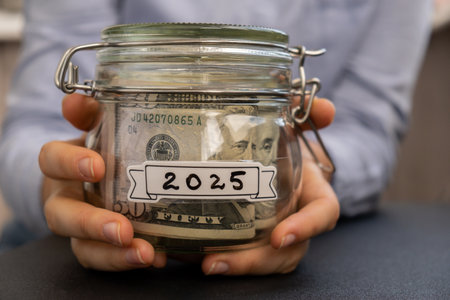 Unrecognizable woman holding Saving Money In Glass Jar filled with Dollars banknotes. 2025 year...