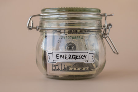 Glass jar full of American currency dollars cash banknote with text EMERGENCY. Preparation saving...