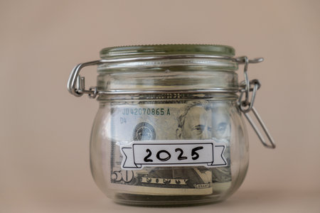 Glass jar full of American currency dollars cash banknote with text 2025 year. Preparation saving...