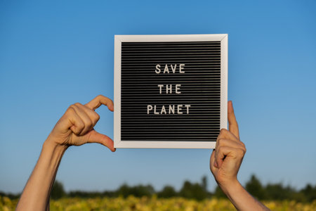 Hands of protester in shape of heart with text SAVE THE PLANET on black board on background of...