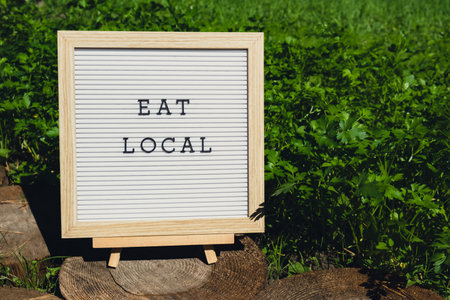 Letter board with text EAT LOCAL on background of garden bed with green herb parsley. Organic farming, produce local vegetables concept. Supporting local farmers. Seasonal marketの写真素材