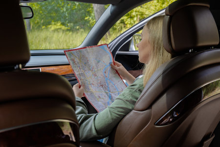 Smiling young woman sitting in car on road check the route on travel map. Local solo travel on...