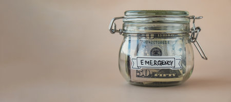 Glass jar full of American currency dollars cash banknote with text EMERGENCY. Preparation saving...