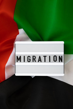 Message MIGRATION on background of UAE flag made from silk. United Arab Emirates national flag with concept of tourism and traveling. Dubai welcoming card. Advertisementの写真素材