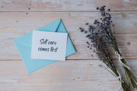 SELF CARE COMES FIRST text on supportive message paper note reminder from blue envelope. Flat lay composition dry lavender flowers. Concept of inner happiness, slowing-down digital detox personal fulfillmentの写真素材