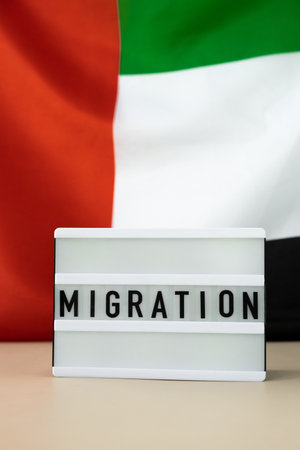 Lightbox with text MIGRATION on background of waving UAE flag made from silk. United Arab Emirates...