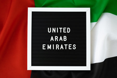Text UNITED ARAB EMIRATES on background waving flag of UAE. National holiday, Independence Commemoration Day Muslim, congratulations. Arabian holidays. Advertisement of Dubaiの写真素材