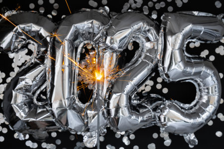 Happy new year 2025 metallic balloons with confetti and sparkler firework Bengal lights on dark black background. Greeting card silver foil balloons numbers Christmas holiday concept. Celebration party congratulationの写真素材