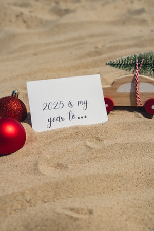 2025 IS MY YEAR TO... text on paper greeting card on background sandy beach sun coast. Christmas balls Santa hat New Year New Me Resolutions decoration. Summer vacation decor. Holiday concept calendar date postcard. Getting awayの写真素材