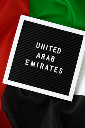 Text UNITED ARAB EMIRATES on background waving flag of UAE. National holiday, Independence Commemoration Day Muslim, congratulations. Arabian holidays. Advertisement of Dubaiの写真素材