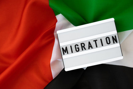 Lightbox with text MIGRATION on background of waving UAE flag made from silk. United Arab Emirates flag with concept of tourism and traveling. Inviting greeting card, advertisementの写真素材