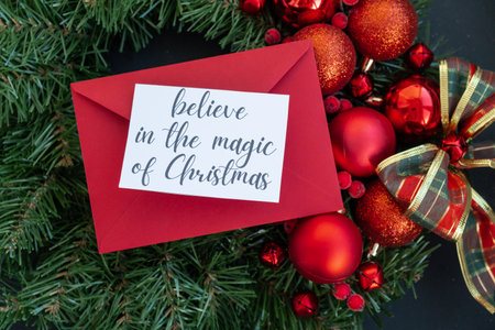BELIEVE IN THE MAGIC OF CHRISTMAS text on postcard with red envelope on handmade Christmas wreath. Zero waste eco-friendly Christmas. Sustainable greeting cardの写真素材