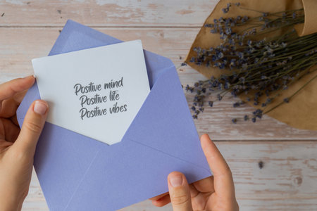 Female hands taking paper card note with text POSITIVE MIND LIFE VIBES from violet envelope....
